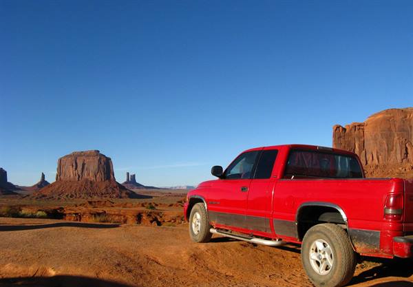 Pickup rossa tra le mesas rosse di Monument Valley a mezzogiorno