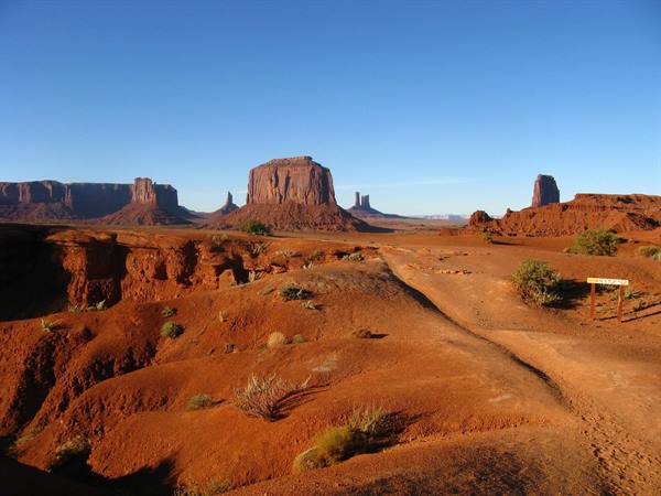 Monument Valley: sentiero sabbioso tra buttes rosse nella luce mattutina