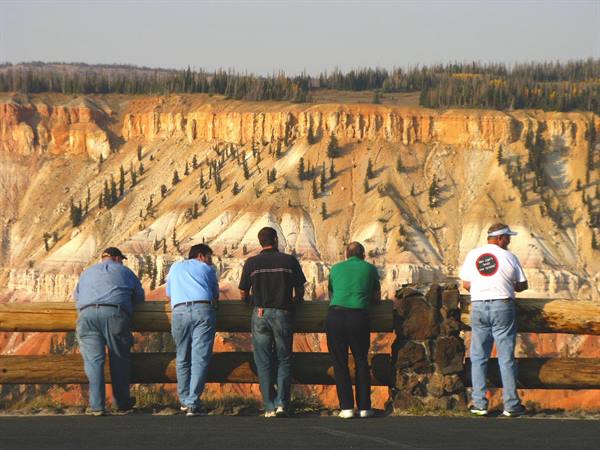 Turisti appoggiati alla staccionata di legno davanti alle pareti rosse di Cedar Breaks
