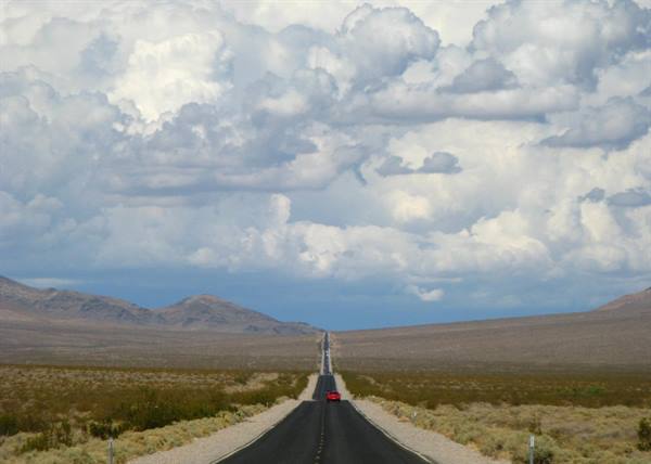 Auto rossa sull'asfalto dritto verso le montagne, cielo di nubi, Death Valley