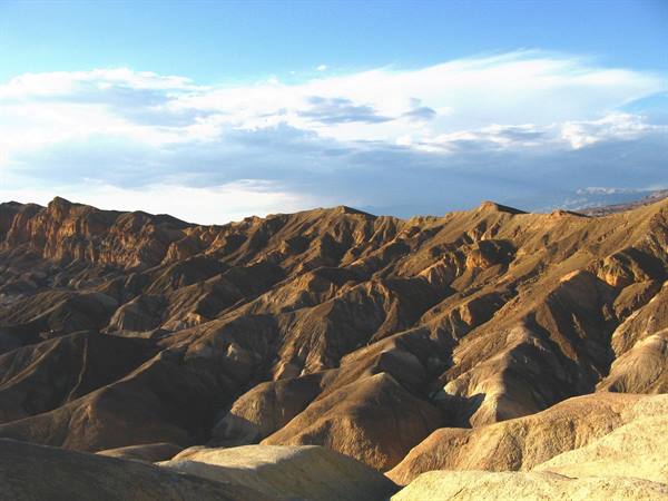Colline erose dorate di Zabriskie Point, Death Valley, sotto nuvole bianche