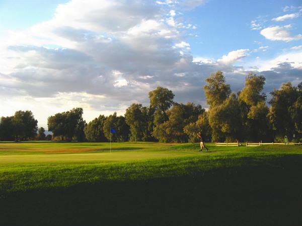 Campo da golf con bandiera blu, giocatore cammina sull'erba verde tra alberi