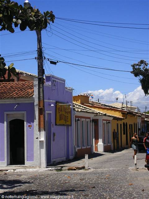 Cobbled street lined with purple and yellow colonial houses under blue sky