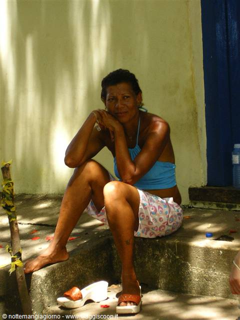 Barefoot woman sitting on concrete steps in the shade, sandals nearby