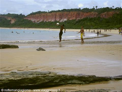 Boys playing football on Pipa beach in front of red cliffs