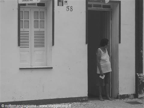 Woman in tank top and shorts standing in doorway, white wall, shuttered window