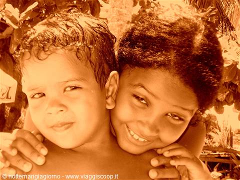 Two smiling children hugging each other, sepia tones, tropical leaves behind