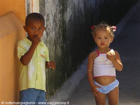 Two toddlers eating snacks beside a dark wall in an alley