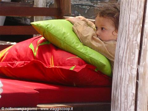 Little girl peeking from red and green pillows between wooden panels
