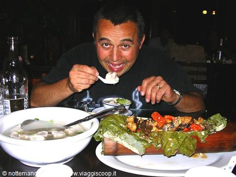 Smiling man eating dumplings with spoon, soup bowl and meat dish on lettuce leaves