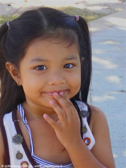 Girl with pigtails smiles shyly with fingers near her mouth