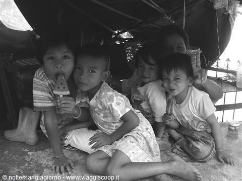 Children sitting on a wooden floor, one licking an ice pop, black and white