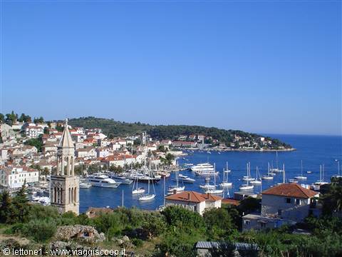 Stone bell tower over Hvar harbor, boats and red roofs under blue sky