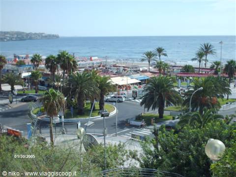Seafront promenade with palms and beach kiosks, cars on avenue, blue sea