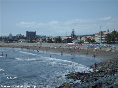 Bathers on sand and shallow water beside rocks, Playa de las Américas