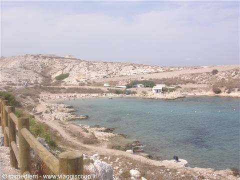 Turquoise bay with rocky beach, wooden fence and dry hills, Lampedusa