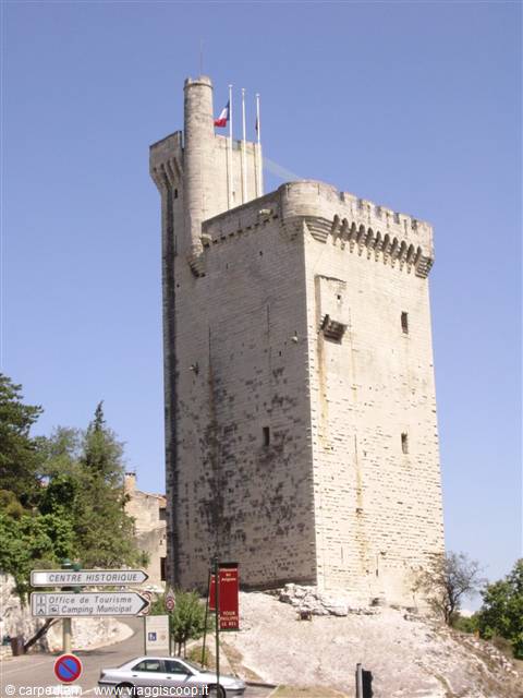 Medieval stone tower with French flag, historic center sign and car below