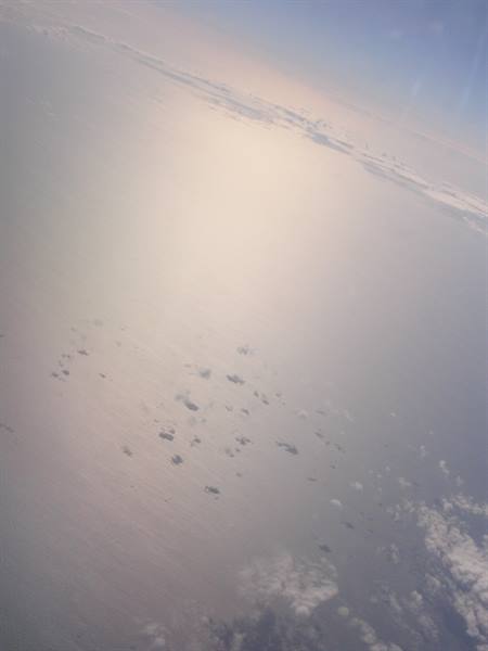 From the plane, sunlight reflecting on the sea among clouds