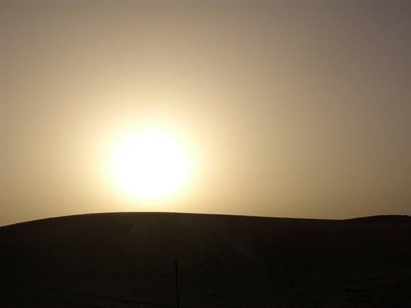 The low sun glows above a dark sand dune in the desert