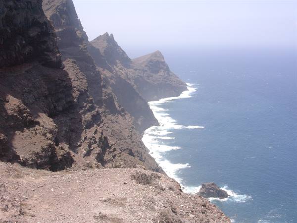 Brown rocky cliffs plunging into blue sea, white foam on waves