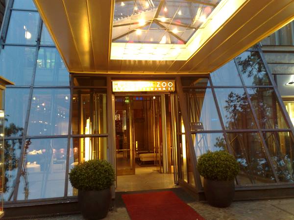 Illuminated glass entrance of the Palace hotel in Berlin, red carpet and potted shrubs