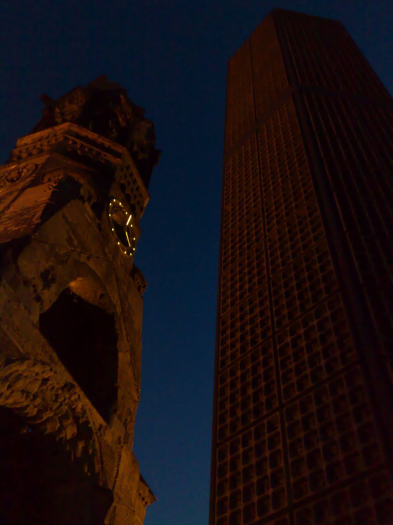Kaiser Wilhelm Memorial Church tower with illuminated clock beside the skyscraper