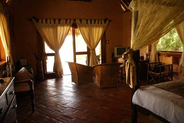 Room with canopy bed, wicker chairs and curtains lit by sunlight