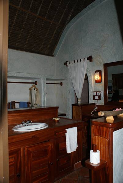 Bathroom with wooden vanity, white sink and thatched roof