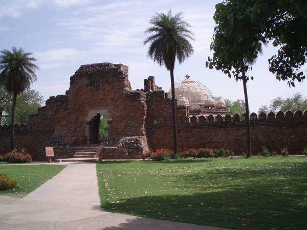Old red stone walls with gateway, domed tomb among palm trees and garden