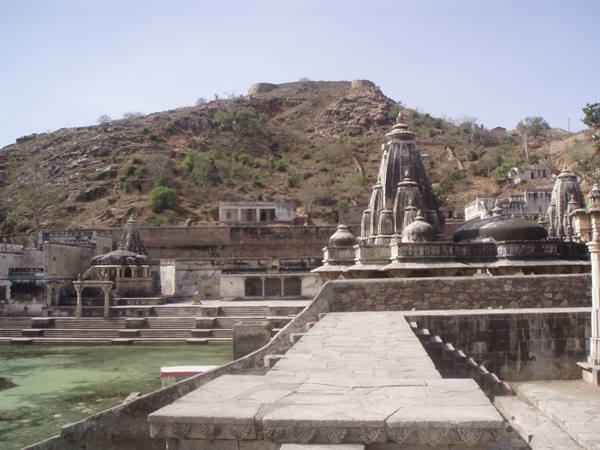 Stone temples with spires by the sacred lake, hill behind