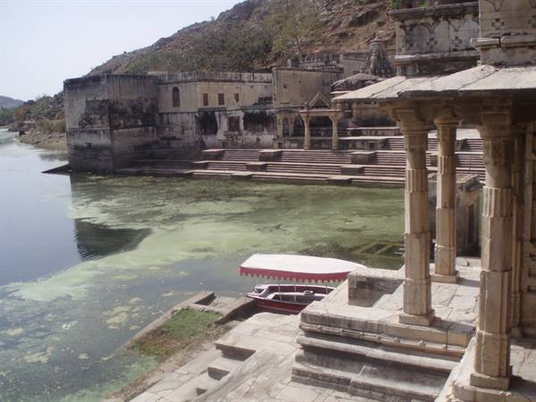 Boats moored by stone ghats on a green lake, orange temples in Bundi