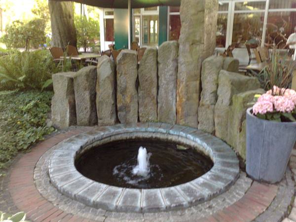 Round stone fountain with water jet, upright stones and pink hydrangeas