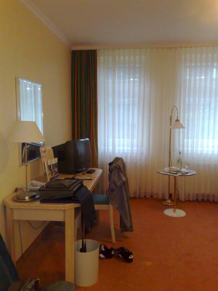 Hotel room with desk, old TV, floor lamp and sheer curtains