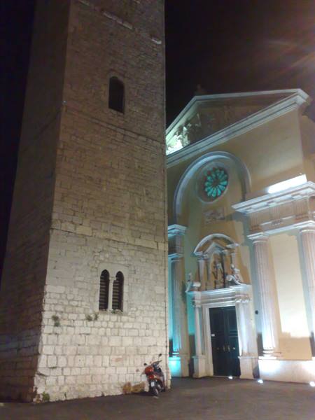 Stone bell tower beside the illuminated church facade with rose window at night