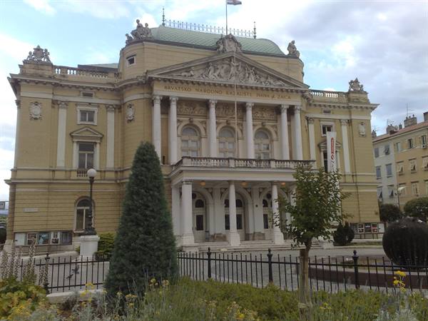 Croatian National Theatre in Rijeka, yellow facade with columns and statues under cloudy sky