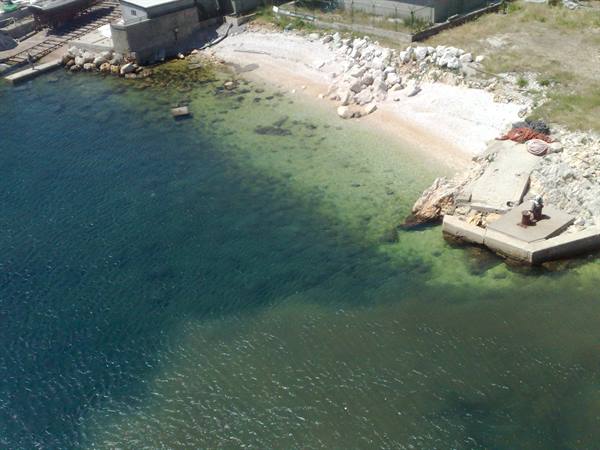 White pebble beach beside concrete pier, clear turquoise sea water