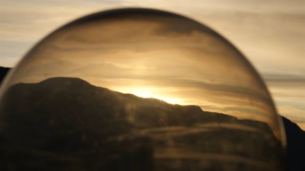 Glass sphere reflecting dark mountains and low sun among clouds