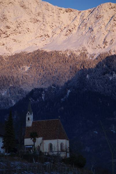 Small church with bell tower beneath snow-covered mountains at dawn