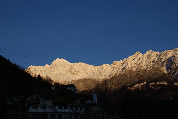 Sunlit snowy alpine peaks above shadowed houses under deep blue sky
