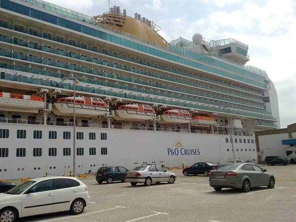 P&O Cruises cruise ship docked, orange lifeboats, cars parked at the port