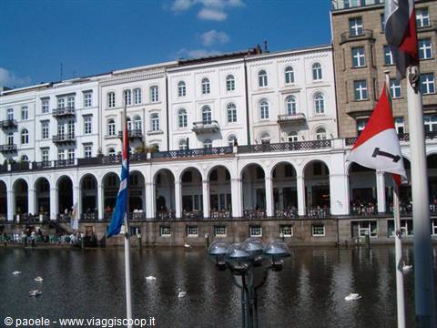 Hamburg's Alsterarkaden, white arcades reflected in the water among flags and swans