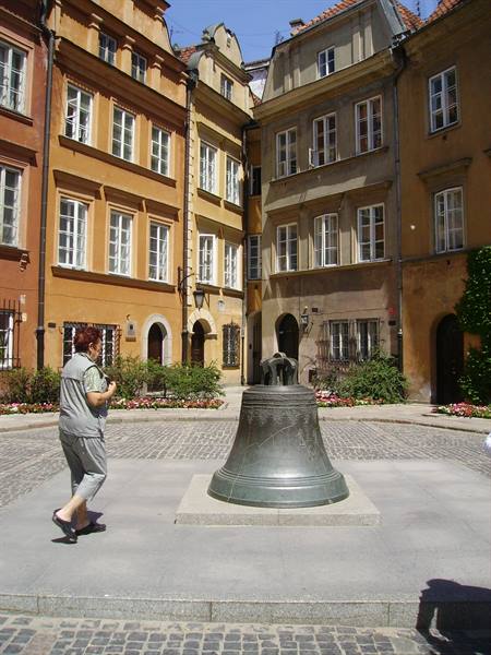 Woman walks beside a large bronze bell in Kanonia Square, Warsaw