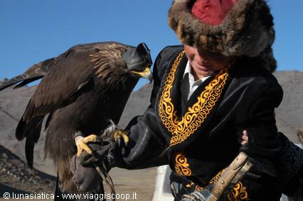 Falconer in fur hat with golden eagle perched on his arm, mountains