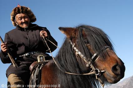 Rider in fur hat on a bay horse with decorated bridle, blue sky
