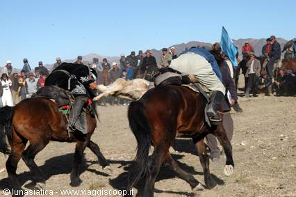Horsemen struggling for the goat carcass in a buzkashi match, crowd on arid hills