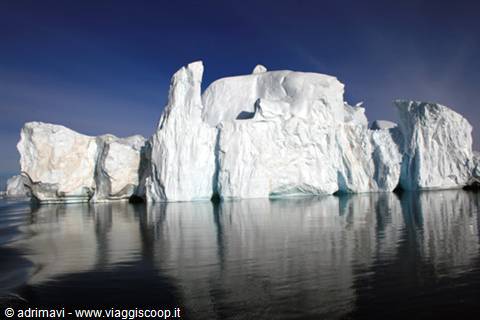 Huge white icebergs reflected in calm water under blue sky