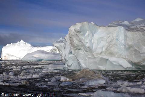 Huge bright icebergs floating among drift ice under a blue sky