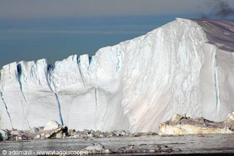 Large white iceberg with jagged walls floating among pack ice