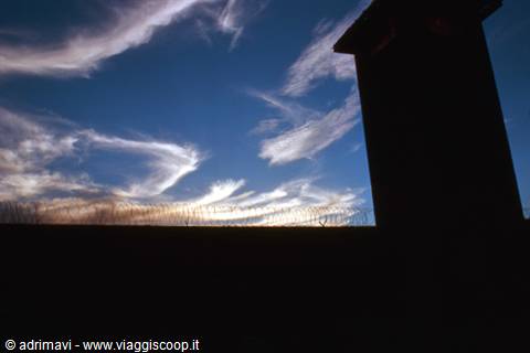 Barbed wire and watchtower silhouetted against white clouds
