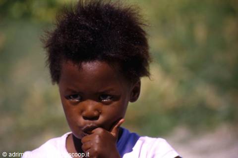 Child with curly hair looks pensive, hand at mouth, sunlight